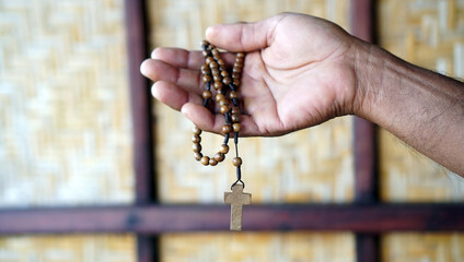 Person holding a wooden rosary in background with light. Praying rosary concept, catholic symbol of devotion to Mother Mary.