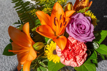 Macro texture background of fresh bright flowers in an indoor florist arrangement, featuring a lavender rose, pink carnation, and an orange lily