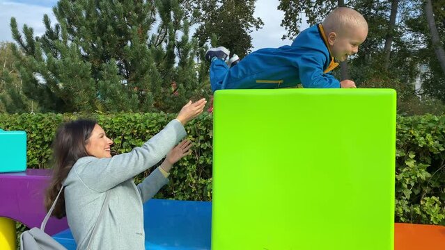 mother with toddler child in amusement park, happy little boy climbing on colorful cubes. Divo Island, St. Petersburg, Russia