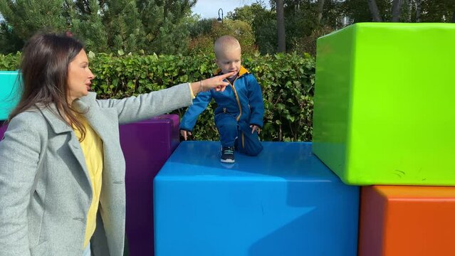 mother with toddler child in amusement park, happy little boy climbing on colorful cubes. Divo Island, St. Petersburg, Russia