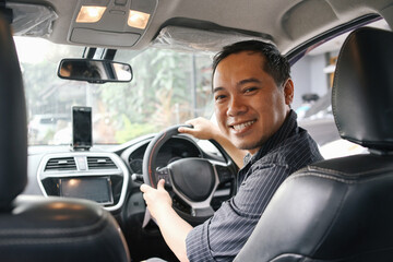 Taxi driver smiling while turning over to the backseat looking talking with clients. - obrazy, fototapety, plakaty