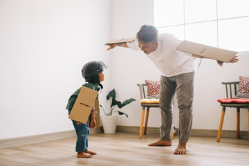 Happy boy with carton plane wings, and cheerful father having fun at home