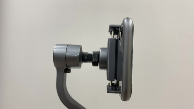 Black automatic gimbal stabilizer holding black phone on table indoor isolated from background. Technology and photography concept 