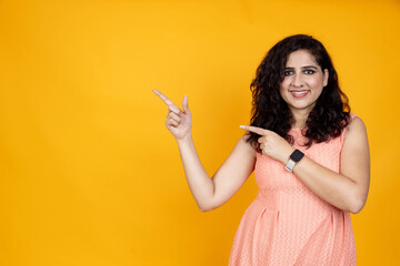Fototapeta na wymiar People emotions, lifestyle and fashion concept. Enthusiastic attractive asian Indian girl pointing right, standing yellow background