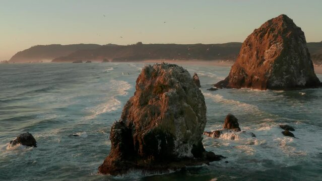 Wide circling aerial shot of a large sea stack surrounded by sea birds