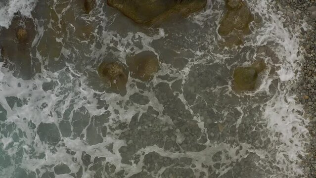 Ocean Waves Crash Over Rocky Boulders Along a Coastal Pebbled Beach with a Top View in Looc Bay, Philippines.