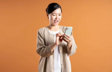 Portrait of middle age Asian woman using phone on brown background