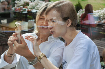 two women, behind glass, looking at photos on their phones, summ