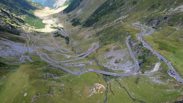 Cars quickly drive switchback winding busy road of Transfagarasan Serpentine highway in romania, under shadow of mountain peaks