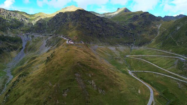 Aerial trucking pan overview of winding Transfagarasan Serpentine Road cutting through vibrant green hillside