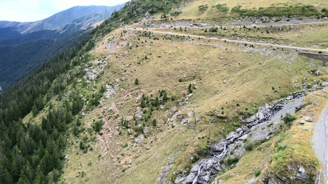Drone rises slowly to balea waterfall, pine tree forest, and winding mountain pass road