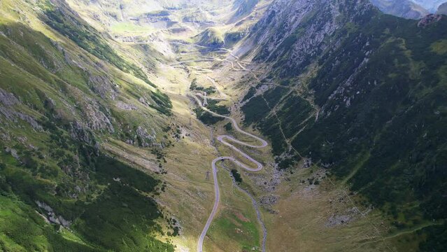 Aerial high panoramic overview of Transfagarasan Serpentine Road as clouds pass shadows over grassy landscape