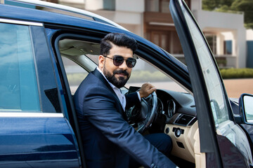 Handsome successful rich wealthy indian businessman in formal wear and sunglasses getting out of luxury car. Multi ethnic, south asian guy lavish lifestyle. Aspirations, Achievements. 