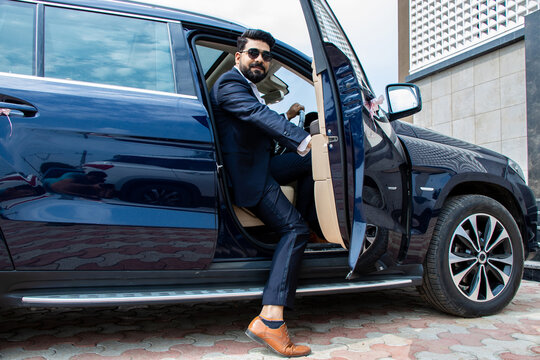 Handsome successful rich indian businessman in formal wear and sunglasses getting out of his luxurious car.