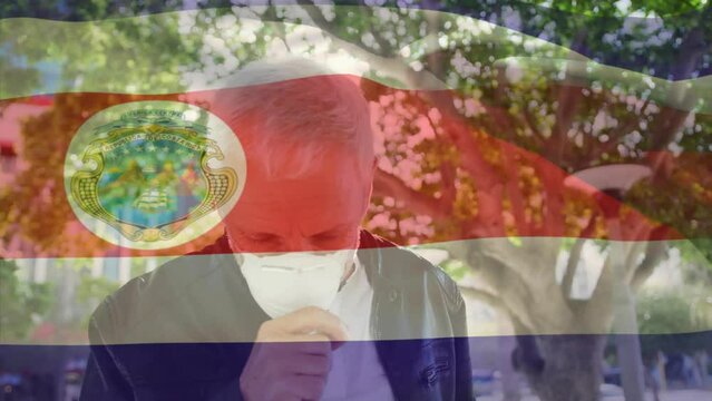 Animation of waving costa rica flag against caucasian man wearing face mask coughing on the street