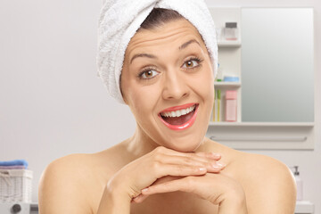 Close-up shot of a young woman with a towel on her head smiling in a bathroom