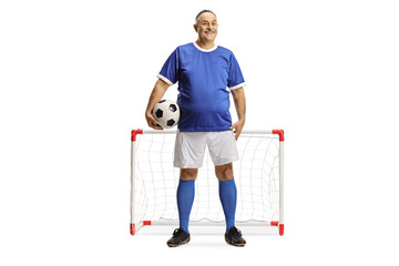 Mature man in a blue football jersey holding a ball and smiling in front of a mini goal