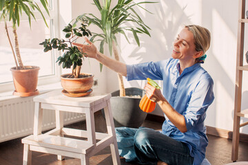Middle aged woman sprays plants in flowerpots at home