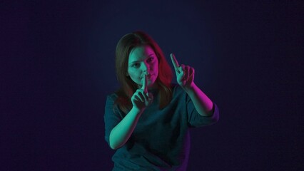 A young woman works on an invisible touch screen. A woman in the studio on a blue background in pink and green neon light. Futuristic technology.