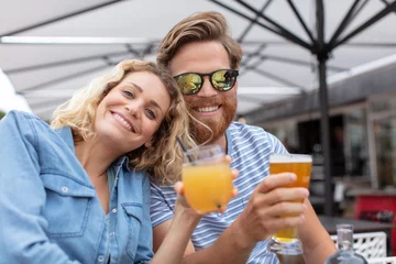 Zelfklevend Fotobehang smiling couple on a terrace holding drinks © auremar