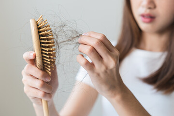 Serious asian young woman holding brush holding comb, hairbrush with fall black hair from scalp...