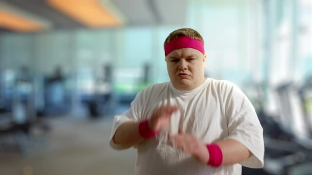 Comic overweight man making funny karate moves against blurred gym background