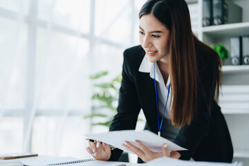 Beautiful young teen asian businesswoman using laptop computer and paperworks with planning working on financial document, tax, exchange, accounting and Financial advisor