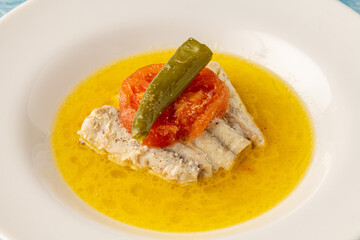 Steamed Sea Bass with peppers and tomatoes on a white porcelain plate