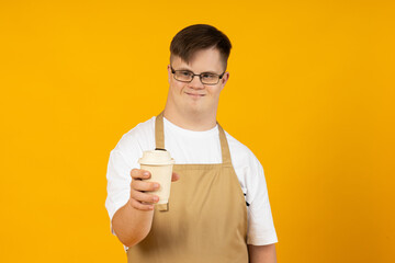 A smiling young man with cerebral palsy in glasses as a barista in an apron and with coffee. World...