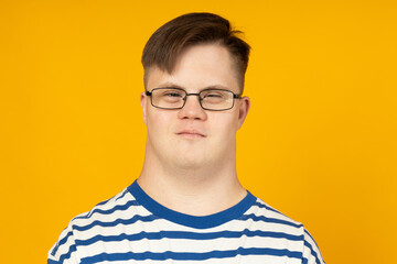 Smiling young man with cerebral palsy in glasses in a striped t-shirt on a yellow background. World Genetic Diseases Day concept