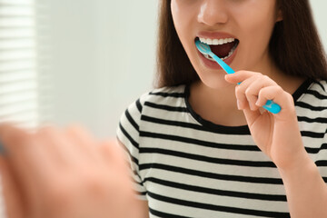 Woman brushing her teeth with plastic toothbrush near mirror in bathroom, closeup