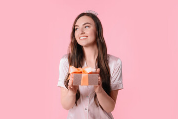 Beautiful young woman in headband holding gift box on pink background. Happy Birthday