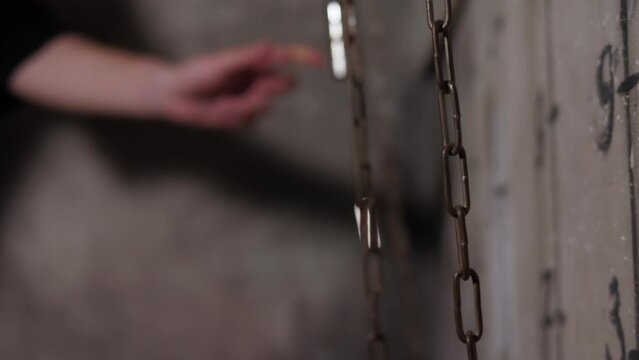 A close-up of a guy moving chains with weights up and down performing a task in the quest room. Dark scary room for a quest.