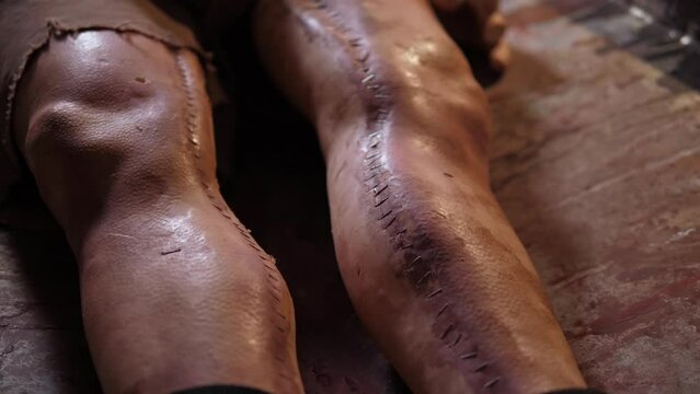 A close-up of creepy bandaged legs with the scars of a plastic mannequin in a panic room or a quest room. A mannequin in the form of a corpse in a creepy room lies on a table with a dirty cloth.