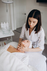 Cosmetologist is wiping woman's face using paper napkins before peeling and massage procedure. Doctor beautician is making beauty procedure in cosmetology clinic. Portrait of young woman, top view.