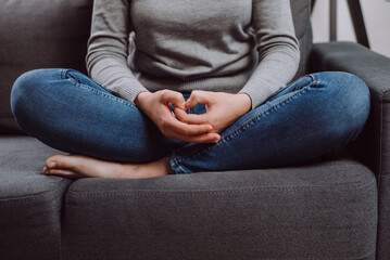 Unrecognizable young caucasian woman folded hands on knees together, sitting on sofa, unhappy female feeling lonely, suffering from domestic violence or relationship problem, break up with boyfriend