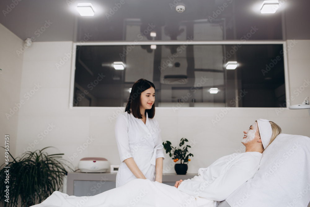 Wall mural skillful cosmetician is making healthy facial mask for client. she is standing and touching brush to