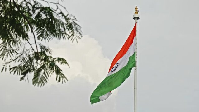 indian flag swaying with clouds in the background and tree branches in the foreground daytime 4k 25p