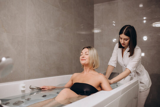 Young woman during hydromassage in beauty salon. Concept of body care and spa. Masseuse massages the girl in the bath with a jet of water. High quality photo