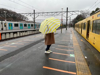 雨が降る西武鉄道の西武球場前駅で黄色い傘をさす後ろ姿の女性