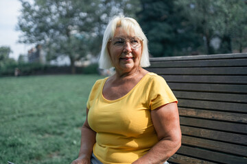 Happy senior woman relaxing on bench in the lawn. Close up face of a mature blonde woman smiling...