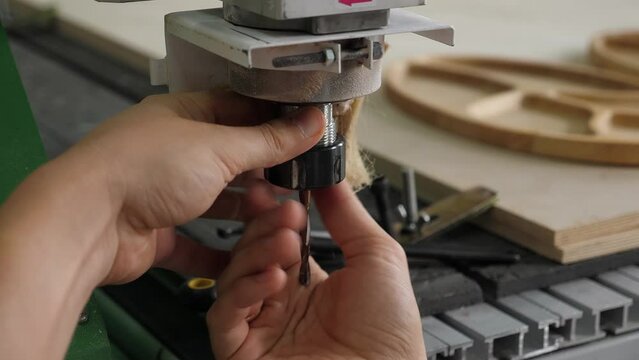 Close-up of a man changing a nozzle with a drill on an industrial wood carving machine. CNC milling machine for cutting wood blanks.