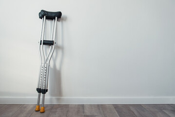 crutches stand near a white wall with copyspace - obrazy, fototapety, plakaty