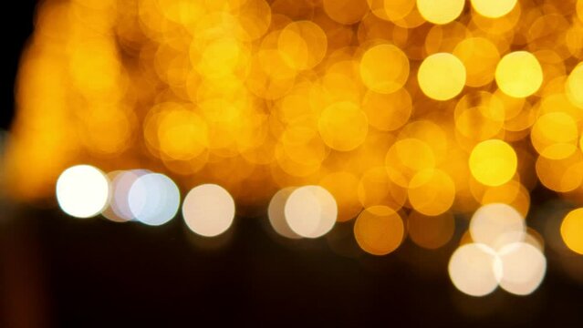 A blurry image of golden lights garlands on trees and roads with cars. Bokeh. Christmas tree decoration along the road.
