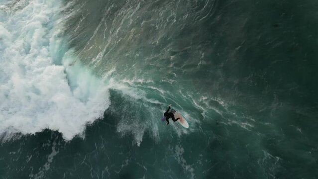 Unrecognizable surfer surfing wave at sunset. Aerial top-down view and slow-motion