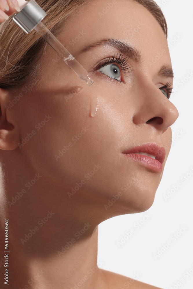 Wall mural Beautiful woman applying cosmetic serum onto her face on white background, closeup