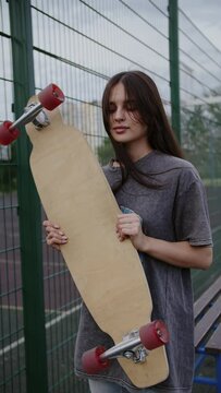 Girl with long hair in the background of the net holding a longboard in her hands, vertical video