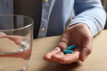 Woman with glass of water and pills at wooden table, closeup