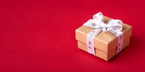 Christmas gift box with white bow on red background. Banner with copy space for text.