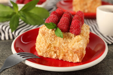 Piece of delicious Napoleon cake with fresh raspberries served on grey table, closeup